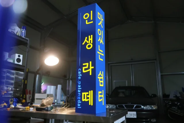 길이 1미터의 3면 돌출 사각 간판입니다. 광확산 PC판 전 후면으로 지정 색상 발광을 위한 조명용 필름, 엠보 무광 불투명 필름, 테두리 보강 및 마감용 테이핑 등 디테일들이  꽤 들어간 사각 돌출형 간판 (큐브간판) 입니다. 

#돌출간판
#큐브간판
#큐브사인
#박스간판
#카페간판

얇은 기둥에 이질감없이 설치하기 위해 기둥 사이즈에 맞고 길이방향으로 길게 제작하였습니다 

무광 엠보 시트가 올라간 광확산 pc판에 아주 약한 레이저커팅으로 글자를 벗겨내서 글자들만 빛낼 준비를 합니다. 

조립완료. 보통 여기까지 해놓으면 거의 다 온것 같은 느낌을 받습니다. 그전까지는 초집중모드라 사진도 잘 없습니다. 

원하는 색상으로 글자가 발광하는지 확인. 조명용필름 +개당 1.5W 의 매우 밝은 5630 led 칩 3구 모듈의 조합. 

테두리 테이핑 마감을 따로 하여 박스 모서리가 빛나지 않도록 해줍니다. 일부러 빛나게 하는것도 나쁜건 아니라 이부분은 취향 차이 입니다.

한판 내 투톤 이상의 컬러 글자가 들어가는건 인쇄가 아닌 방식으로 제작할 때 두배로 손이 가는 작업입니다. 대신 일반적으로 인쇄한 실사출력 시트를 면에 부착하는 방식보다 비교할수 없이 쨍 하지요. 

완성 후 불을 꺼두고 여러각도에서 사진을 찍어봅니다

주문 주신 고객분께 완성되었다고 전달드릴 사진도 몇장 찍어둡니다. 오늘의 미션 완료🙏